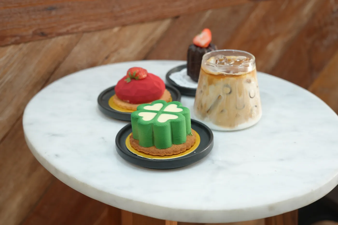 Individual cakes and an iced latte on a marble table.
