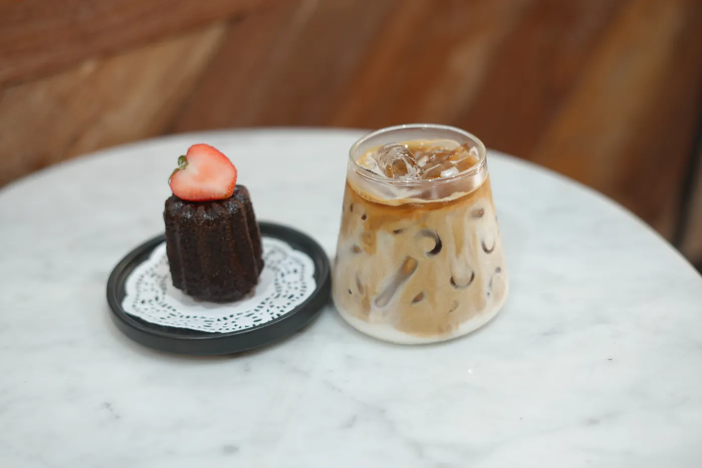 A canele with a strawberry beside an iced latte.
