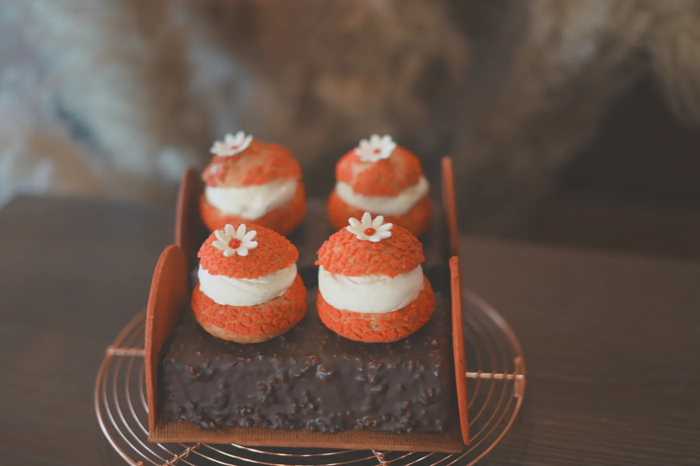 Four choux puffs with orange crumble tops on a chocolate slab.