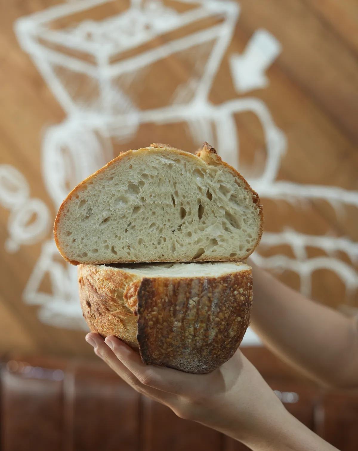 A sourdough loaf cut in half and held up, its open crumb facing the camera.