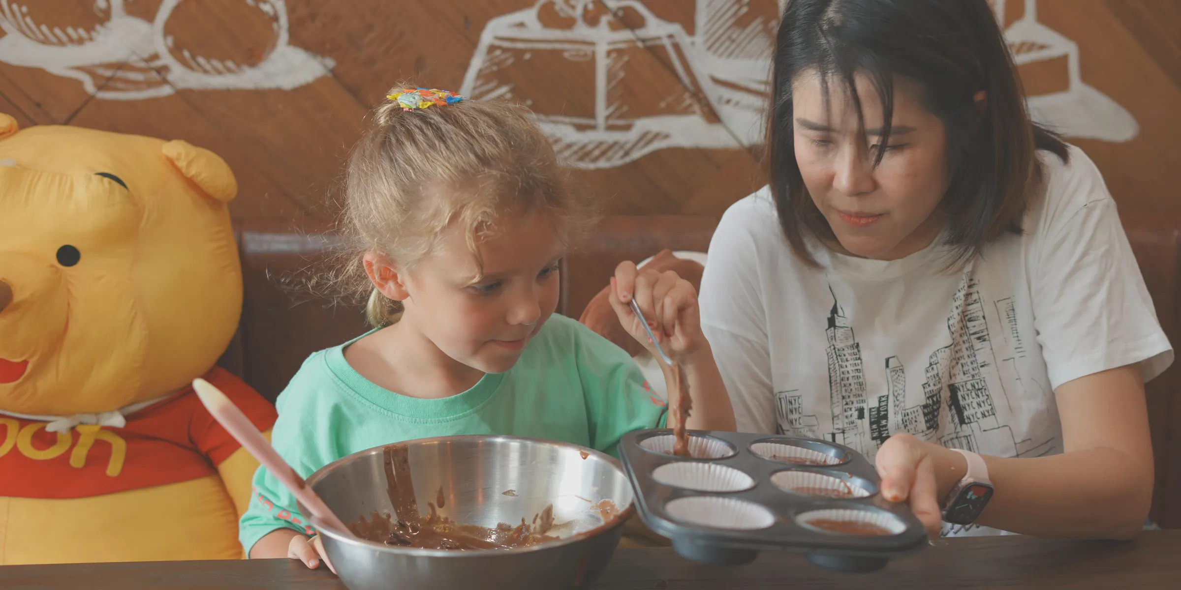 A teacher and a young student filling cupcake cases together in a baking class at Ray.