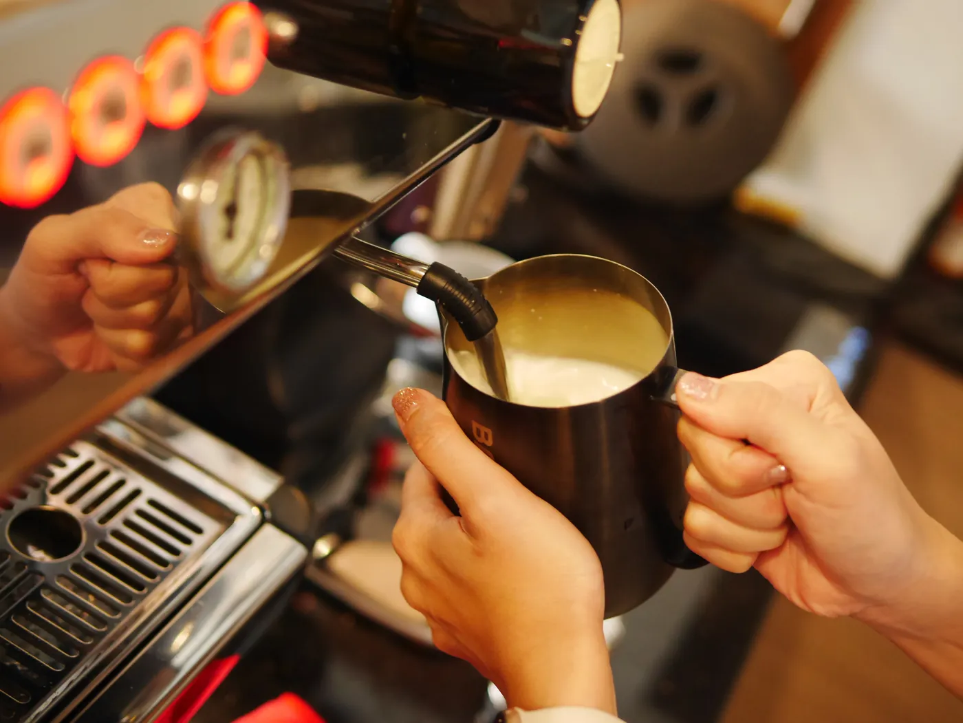 A barista's hands steaming milk at the espresso machine.