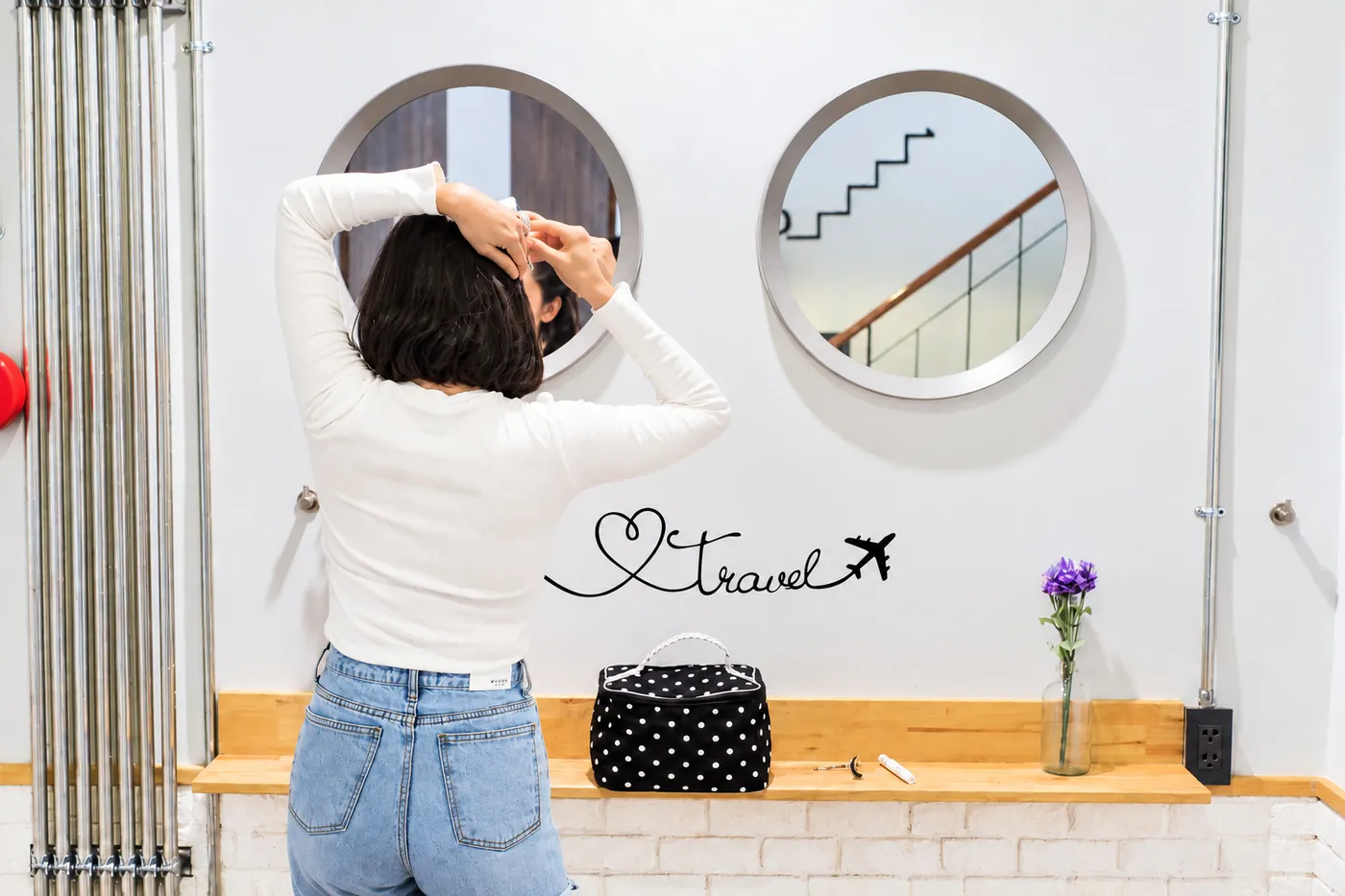 A guest doing her hair at the shared vanity, two round mirrors and a travel sign on the wall.