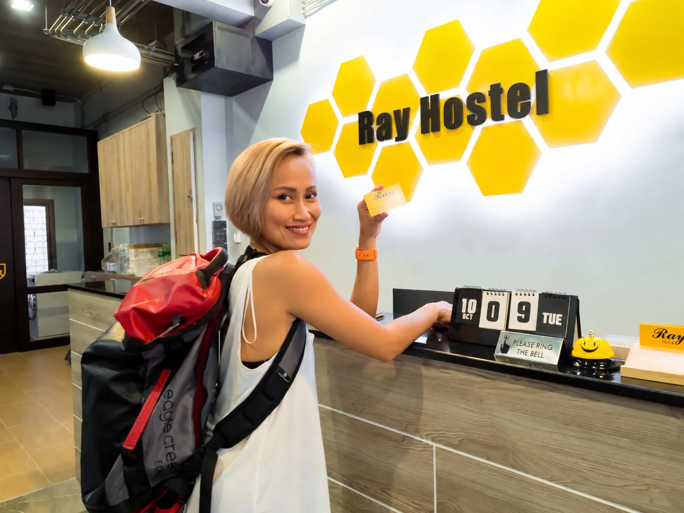 A guest smiling with her key card at the reception, under the Ray Hostel sign.