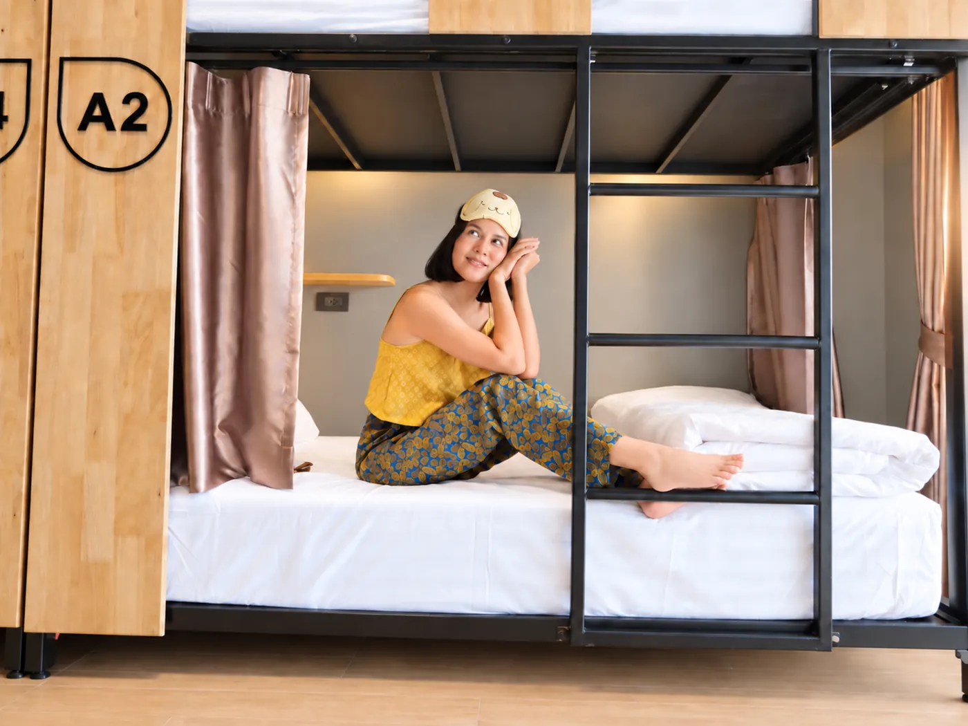 A guest smiling on bed A2 with her sleep mask up.
