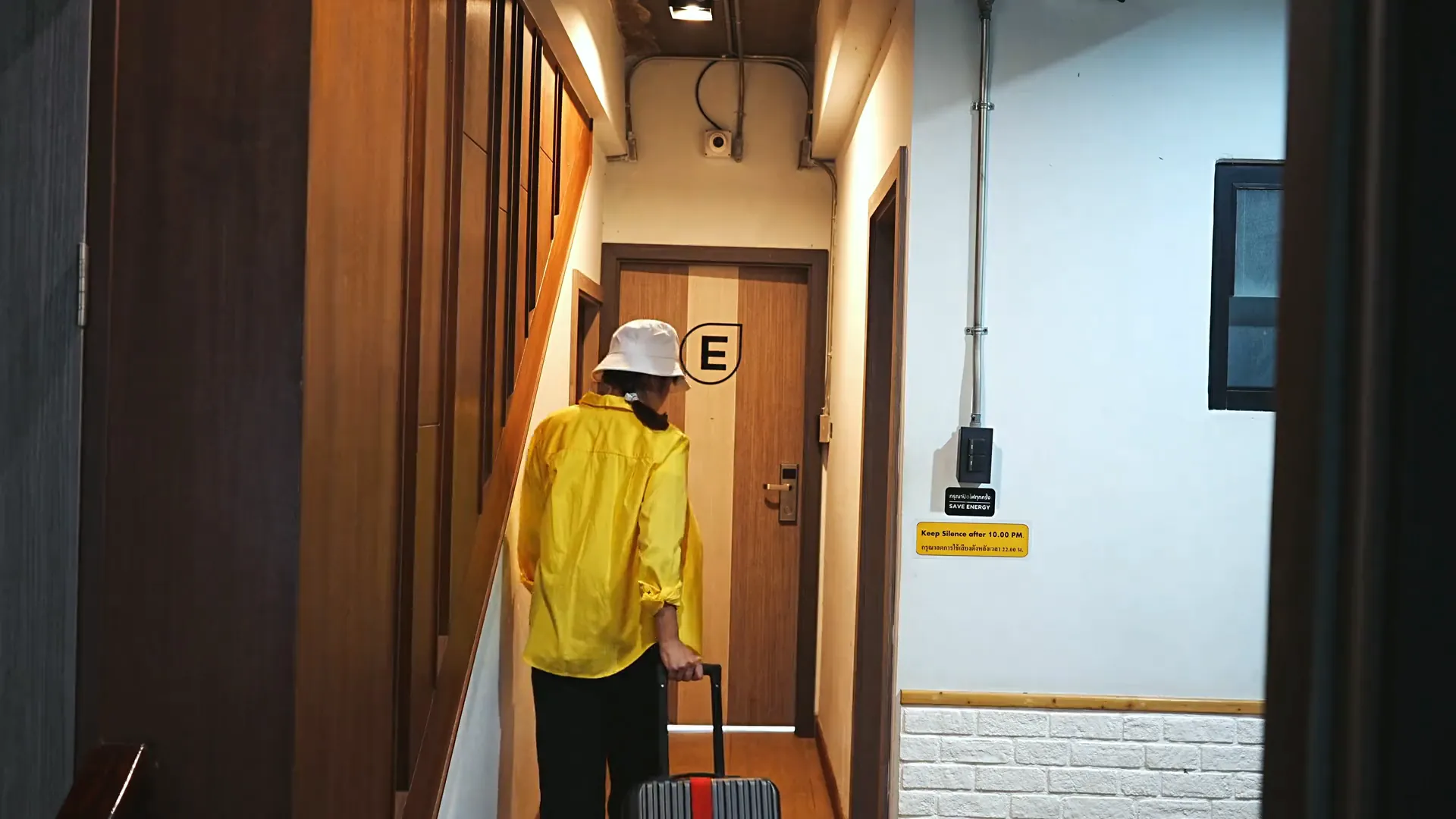 A guest in a yellow jacket wheeling her suitcase down the corridor to room E.
